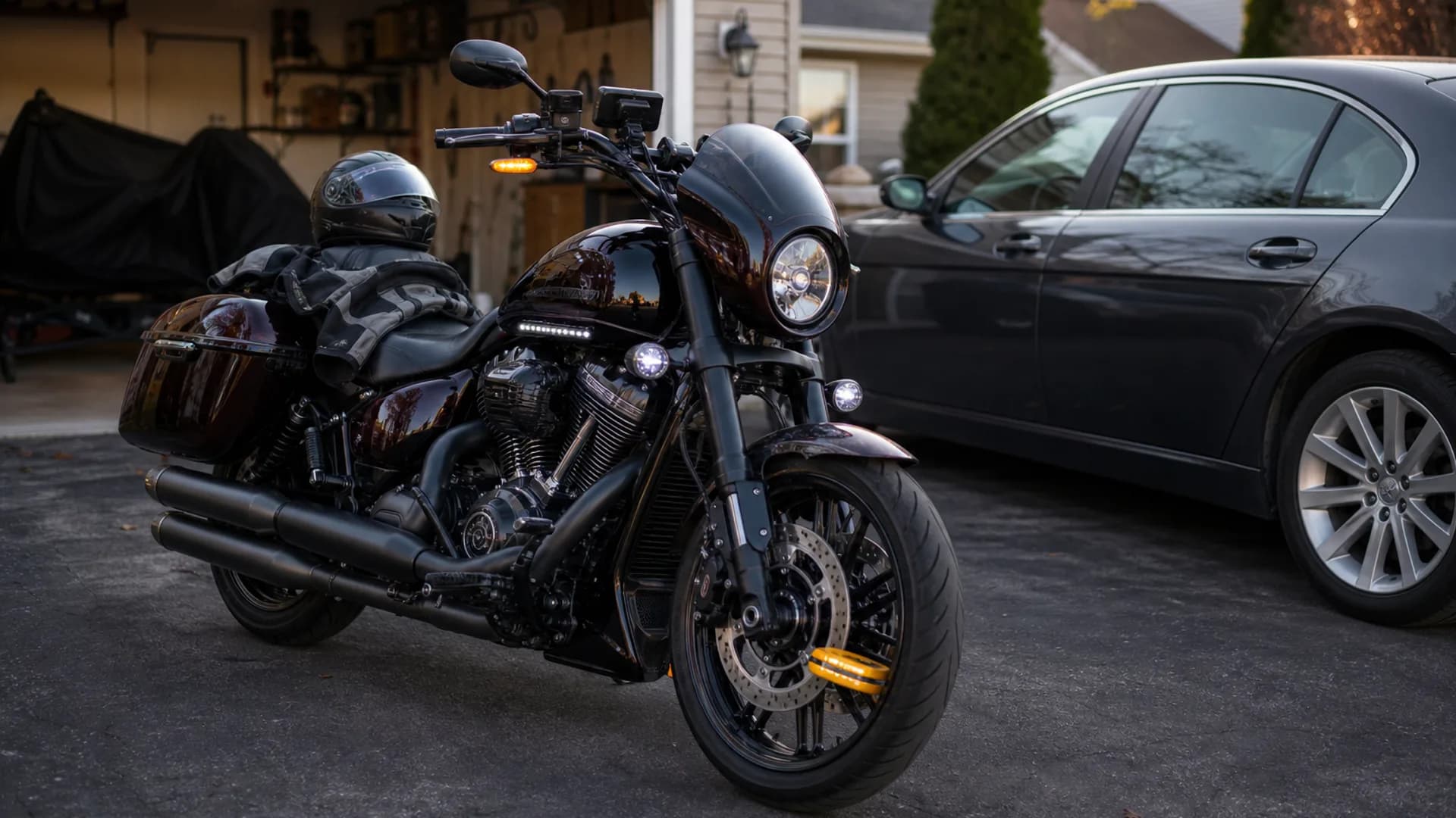 Street cruiser motorcycle in a suburban driveway with helmet, riding jacket, disk lock, and a parked car